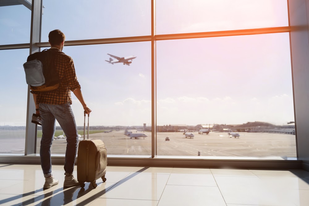 Person with luggage looking out the window watching a plane take off